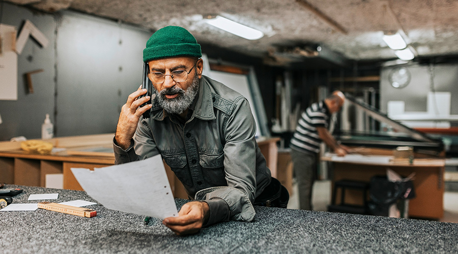 A businessman in a crafty office setting talks on his mobile phone looking at a sheet of paper.