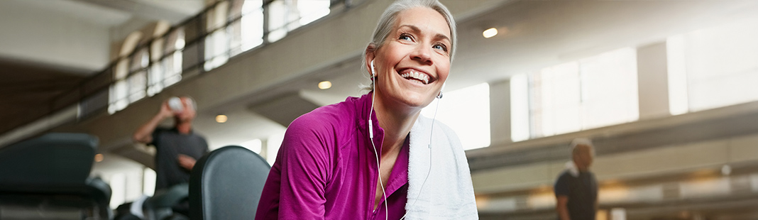 A woman smiles while listening to earbuds after completing a workout.