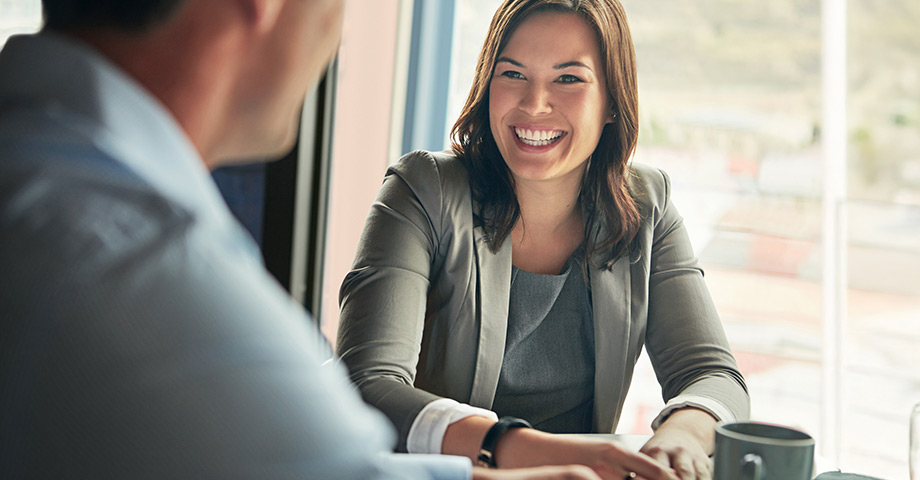 A well-dressed woman smiling while speaking with a colleague in a professional office setting.