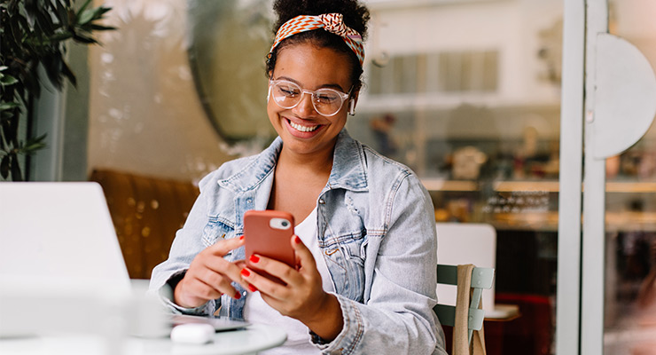 Young smiling woman sits at table talking to therapist on her mobile phone.