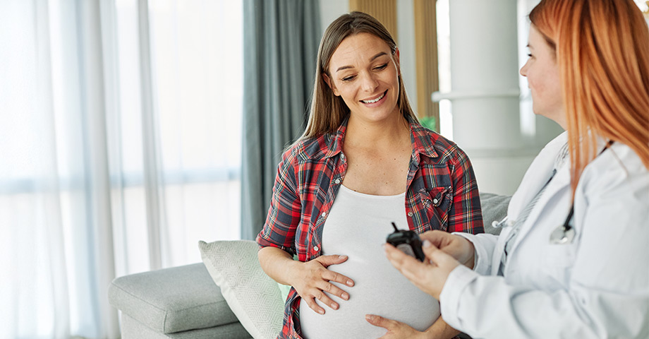 Pregnant woman holds her belly while listening to her doctor.