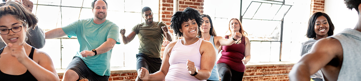 Group of smiling men and women exercise together doing aerobics in a fitness studio.