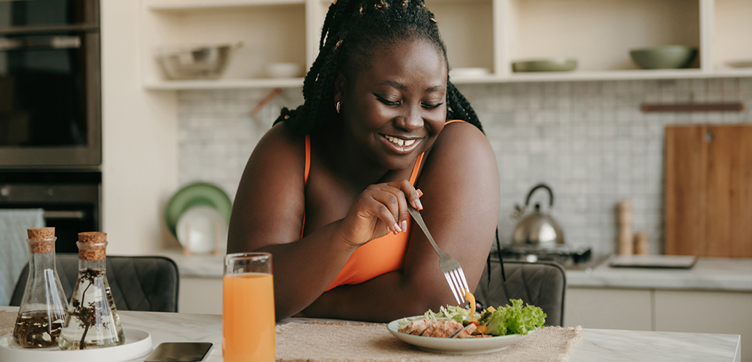 Woman smiling while eating a salad with a glass of juice