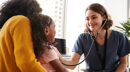 Female doctor checking a young girl’s heartbeat while her mother holds her in a bright office, highlighting compassionate care that supports children’s health.