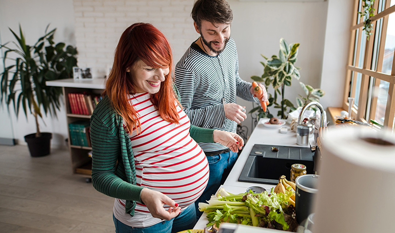 Smiling couple prepares vegetables together in their kitchen, representing birth doula support for PEBB members during pregnancy and postpartum.