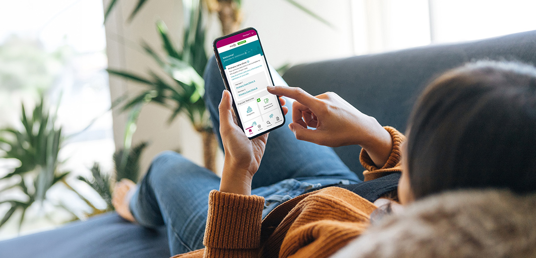 Woman uses Moda 360 health programs on her smartphone at home, supporting personalized wellness and healthier everyday choices.