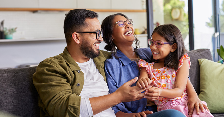 A couple relaxes with their young daughter on a couch, showing family comfort and peace of mind that come from dependable health coverage and care.
