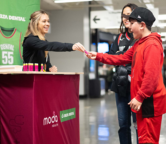 A female Moda Health rep hands Chapstick to a smiling young boy.