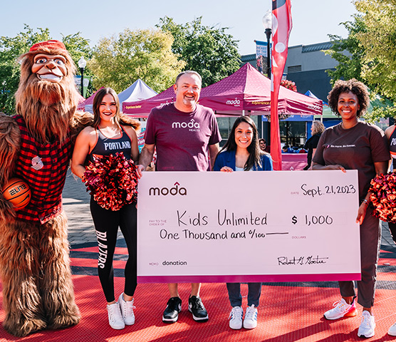 Moda Health and Portland Trail Blazers team reps hold a large check at a community event.