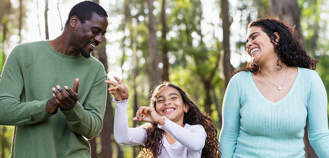 A young couple laugh and play with their daughter on a woodsy hiking trail.