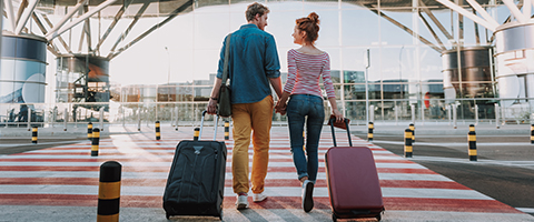 A could with suitcases walking to an airport, hand-in-hand